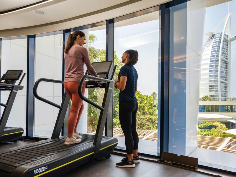Zwei Frauen im Fitnessstudio an Laufband mit großer Fensterfront und Blick auf Burj Al Arab.