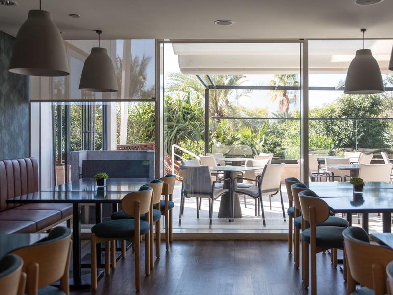 Moderner Gastraum mit Holztischen und Stühlen, offenem Zugang zur Terrasse mit Außensitzplätzen.