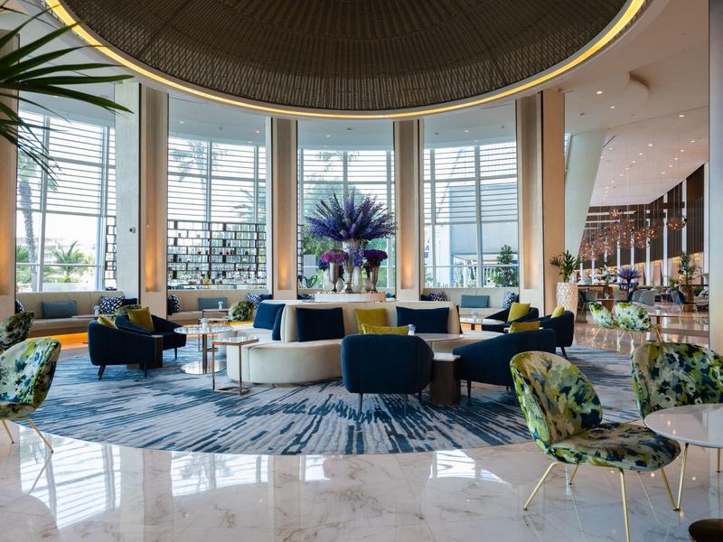 Großer, heller Hotel-Lobbybereich mit modernen Sesseln, Teppich, Pflanzen und großen Panoramafenstern.