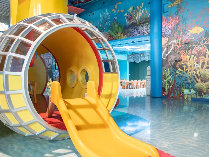 Buntes Indoor-Spielgerät mit runder Rutsche in einem Meeres-Themenraum mit Fisch- und Korallenbildern.