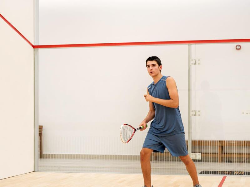 Junger Mann in blauem Sportoutfit mit Squashschläger in heller Squashhalle.