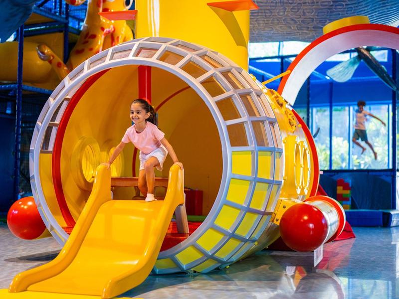 Kinder spielen in einer bunten, runden Rutschbahn im Innen-Spielplatz.