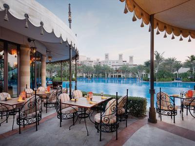 Außenbereich eines Cafés mit Stühlen und Tischen, Blick auf Wasser und Stadt im Hintergrund.