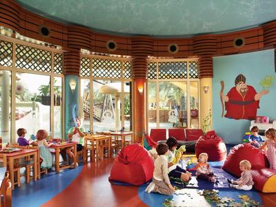 Ein runder, bunter Raum mit großen Fenstern, kindgerechten Möbeln und spielenden Kindern.