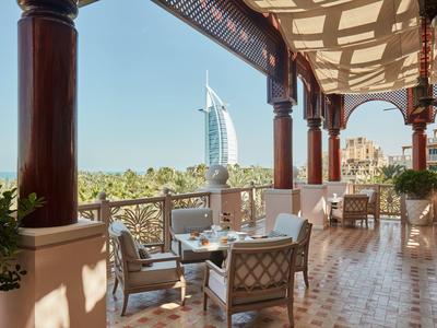 Terrassenbereich mit Stühlen, Tischen und Säulen, im Hintergrund Burj Al Arab bei klarem Himmel.