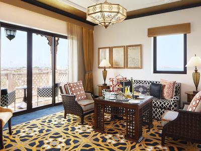 Helles Wohnzimmer mit großem Fenster, gemustertem Teppich und dunkelbraunen Möbeln aus Holz.