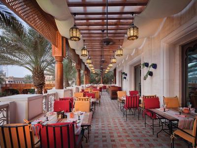 Überdachte Hotelterrasse mit bunten Sesseln und Tischen entlang eines Flurs unter Laternen.