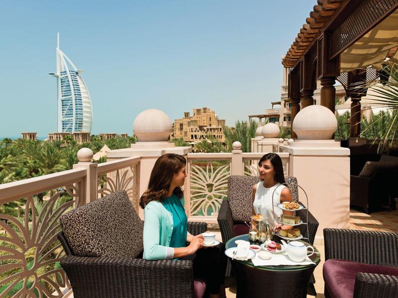 Zwei Frauen sitzen an einem Tisch auf einer Terrasse mit Blick auf das Burj Al Arab Hotel.
