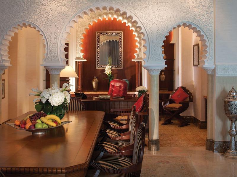 Innenraum mit dekorativem Holztisch, bunten Polsterstühlen und dreiteiligen Bögen im arabischen Stil.