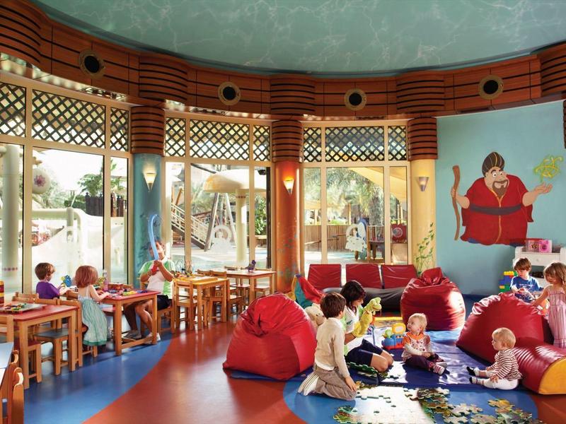 Ein runder, bunter Raum mit großen Fenstern, kindgerechten Möbeln und spielenden Kindern.