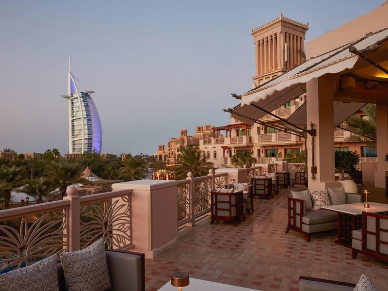 Terrassenbereich mit Sitzmöbeln und Blick auf den Burj Al Arab bei Sonnenuntergang in Dubai.