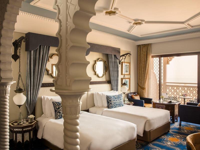 Elegantes Hotelzimmer mit zwei großen Betten, dekorativen Säulen und warmem Licht.