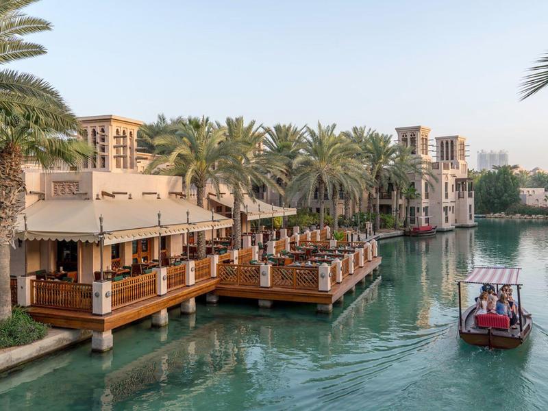 Traditionelle arabische Gebäude am Wasser mit Holzterrassen und einem kleinen Boot auf dem Kanal.