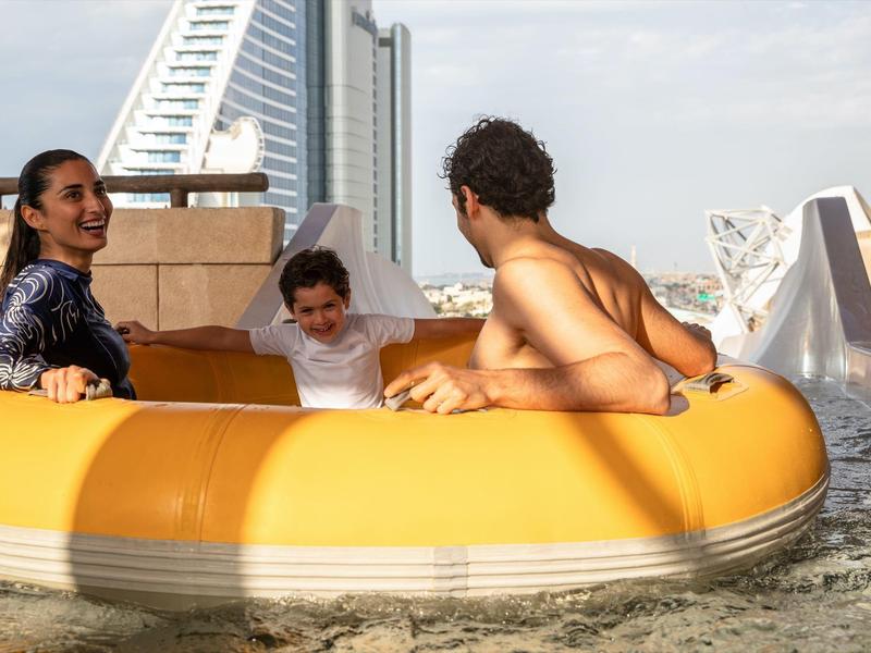 Drei Personen sitzen in einem gelb-orangenen Schlauchboot auf ruhigem Wasser bei bewölktem Himmel.
