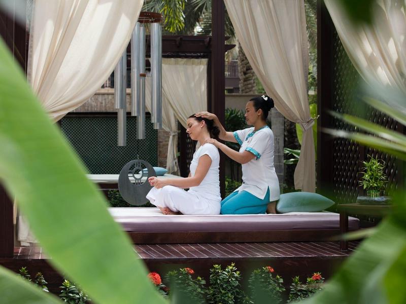 Frau erhält Rückenmassage im offenen Pavillon mit Vorhängen, umgeben von grünen Pflanzen.