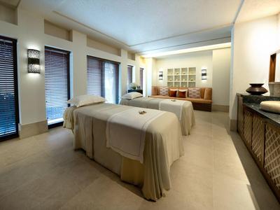 Helles Spa-Zimmer mit zwei Massagebetten, großen Fenstern und moderner Holzmöblierung.