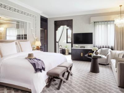 Modernes Hotelzimmer mit großem Bett, Sitzbereich, Fernseher und eleganter Beleuchtung in neutralen Tönen.