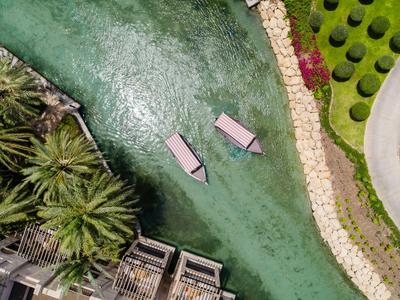 Zwei Liegen im klaren Wasser neben Palmen und gepflegtem Garten in tropischem Resort.