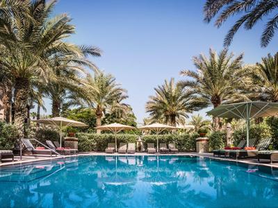 Ein klarer blauer Pool umgeben von Palmen und Liegestühlen unter blauem Himmel.