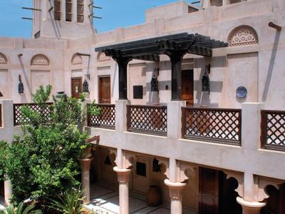 Traditioneller Innenhof mit Pflanzen, Holzmöbeln und hellen, hohen Gebäuden unter blauem Himmel.