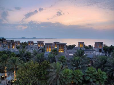 Blick auf Palmen und Hotels bei Dämmerung mit rosafarbenem Himmel und Meer im Hintergrund.