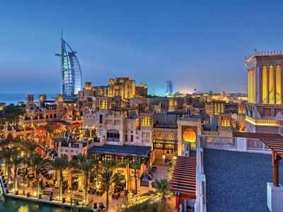 Blick auf Dubai bei Abenddämmerung mit beleuchteten Gebäuden und Burj Al Arab am Wasser.