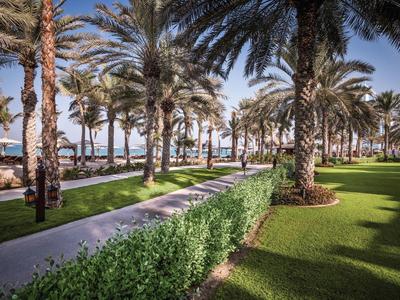 Palmengarten mit saftig grünen Wiesen, gewundenem Weg und klar blauem Himmel am Strand.