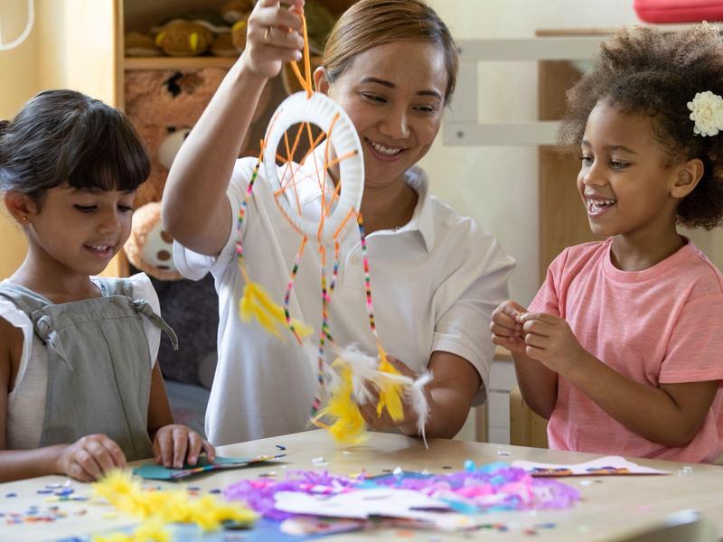 Drei Mädchen basteln zusammen mit bunten Bastelmaterialien an einem Traumfänger.