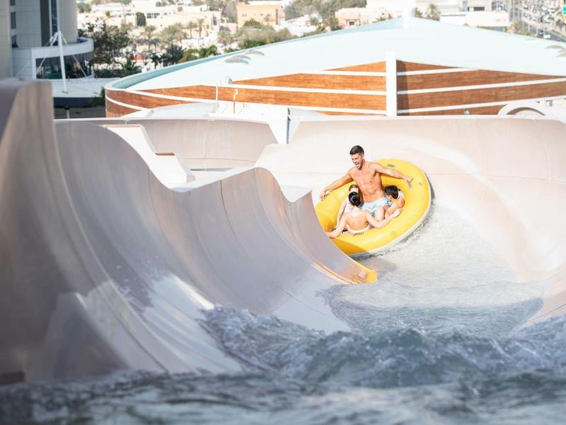 Person fährt in einem gelben Schlauchboot eine breite, weiße Wasserrutsche hinunter.
