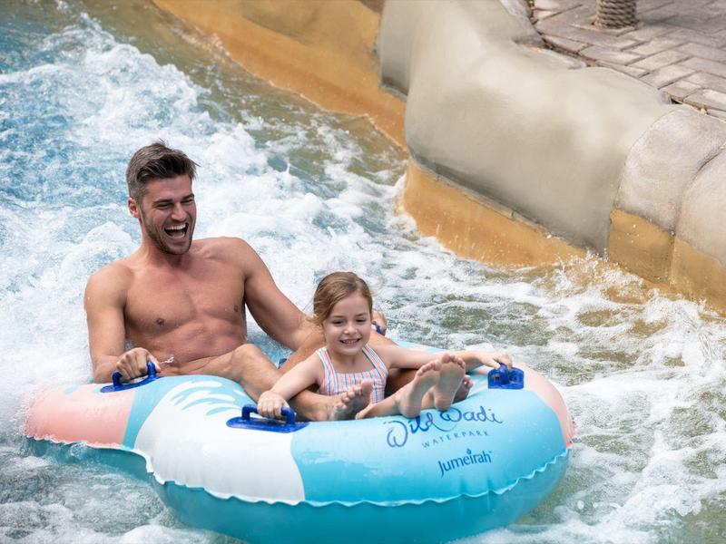 Ein Mann und ein Mädchen fahren gemeinsam in einem blauen Reifen den Wasserfluss hinunter.