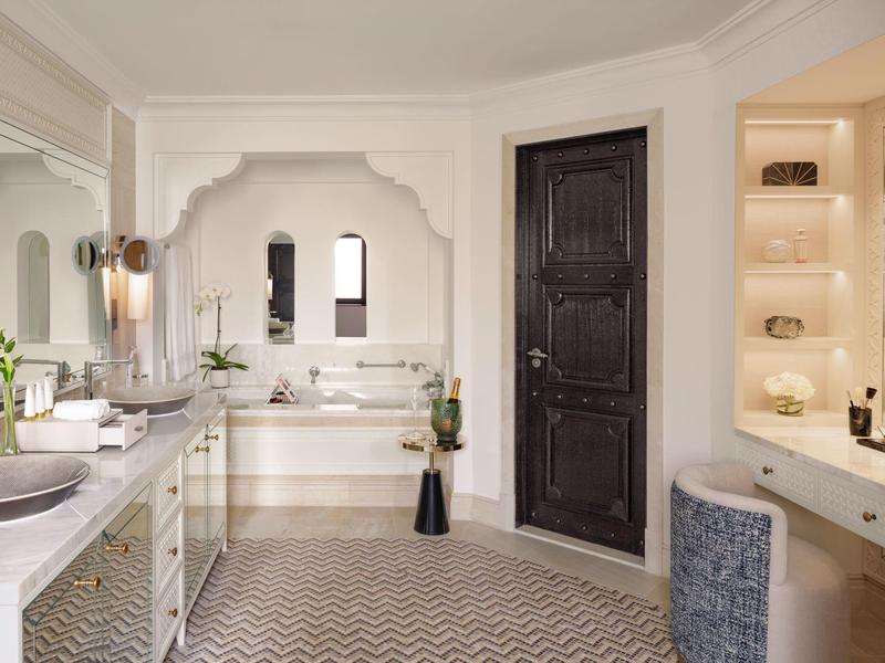 Helles Badezimmer mit großer Badewanne, dunkler Holztür und hellen Fliesen in Zickzackmuster.