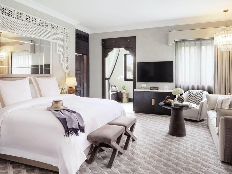 Modernes Hotelzimmer mit großem Bett, Sitzbereich, Fernseher und eleganter Beleuchtung in neutralen Tönen.