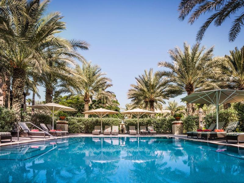 Ein klarer blauer Pool umgeben von Palmen und Liegestühlen unter blauem Himmel.