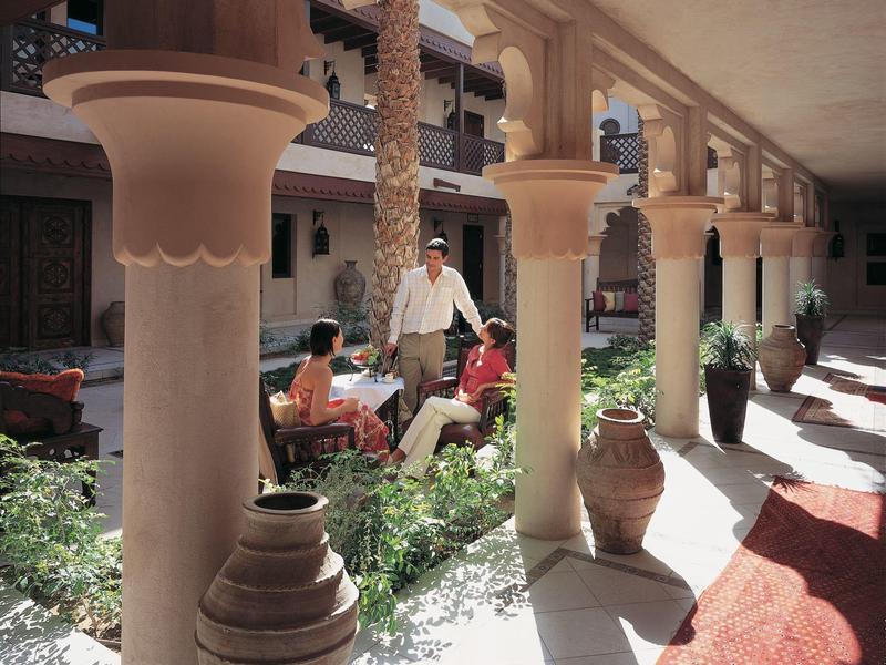 Innenhof mit Säulen, Palmen, Pflanzen, Sitzgruppe und warmem Licht, traditionelle Architektur.