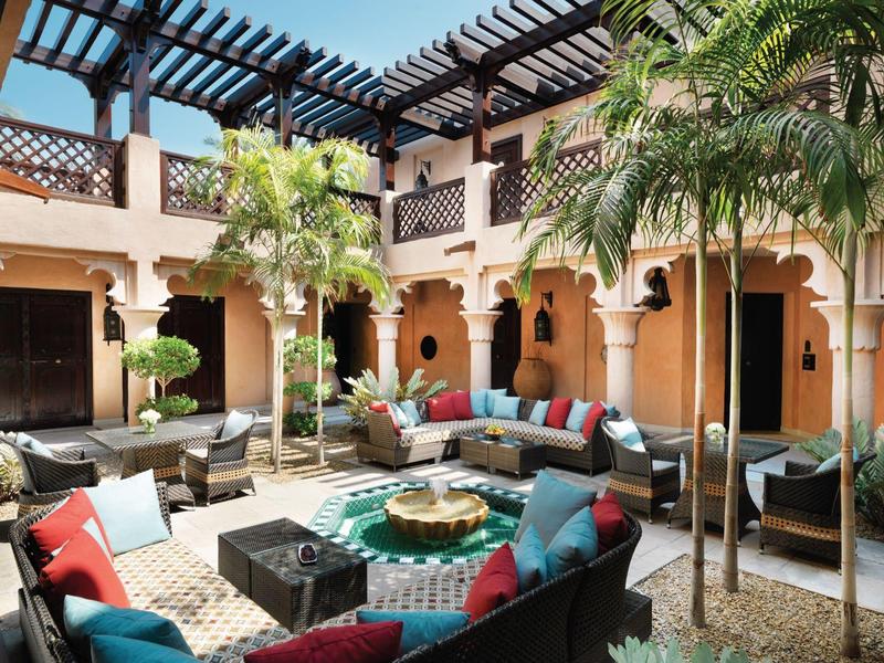 Innenhof mit gepolsterten Sofas, bunten Kissen, Palmen und traditionellen Bögen in warmen Tönen.