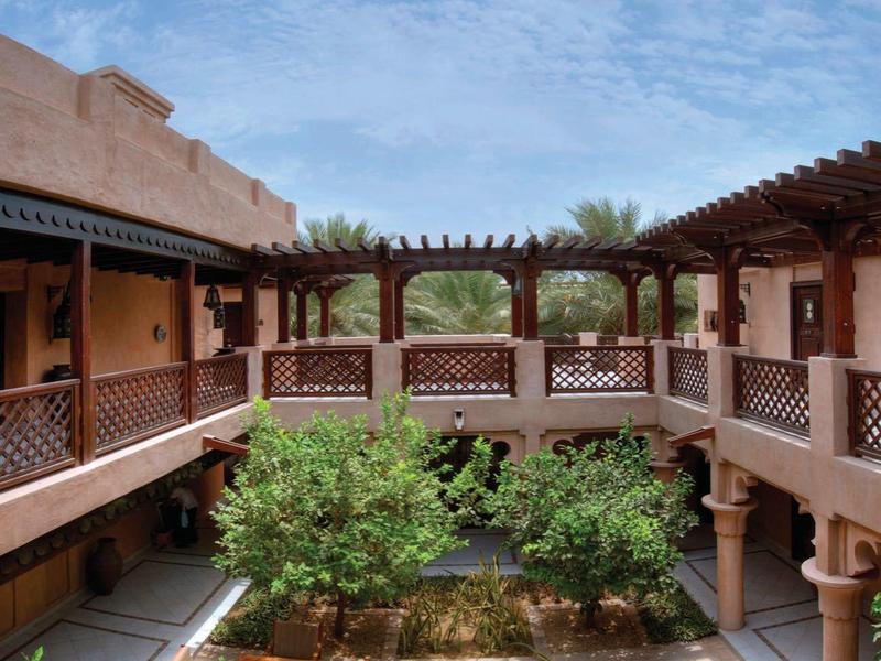 Innenhof mit Springbrunnen, umgeben von zweistöckigen Gebäuden mit Holzbalkonen und üppigem Grün.