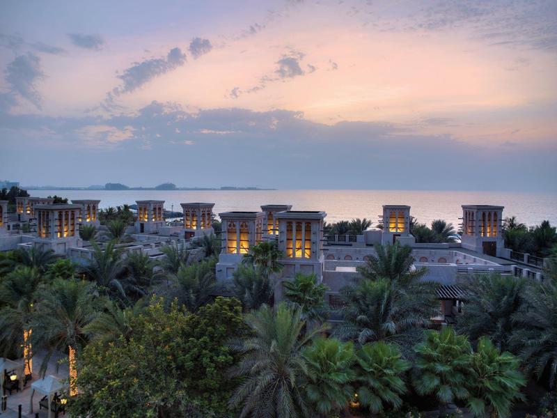 Blick auf Palmen und Hotels bei Dämmerung mit rosafarbenem Himmel und Meer im Hintergrund.