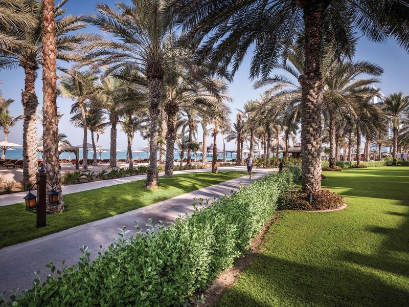 Palmengarten mit saftig grünen Wiesen, gewundenem Weg und klar blauem Himmel am Strand.