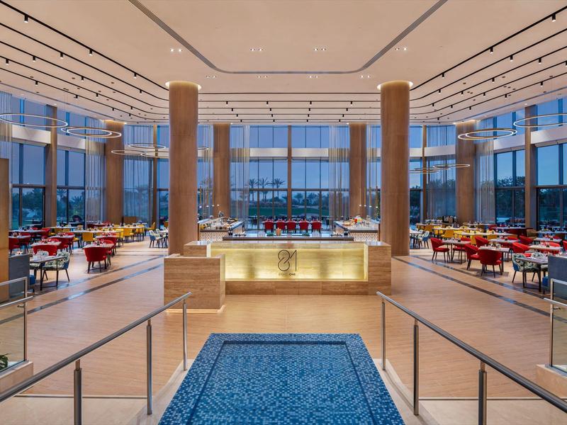 Großes modernes Restaurant mit vielen roten Stühlen, blauen Teppichen und breiten Säulen.