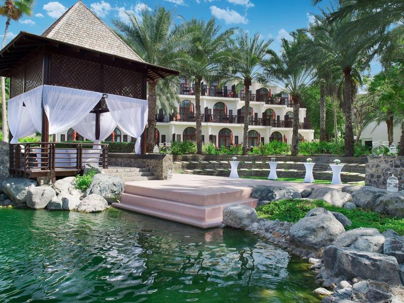 Ein Resort mit Pavillon, Springbrunnen, Felsen und Wasserbecken, umgeben von Palmen.