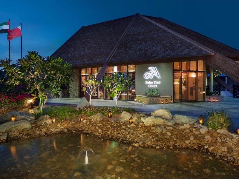 Modernes Gebäude mit spitzem Dach, beleuchtet bei Nacht, vor einem Teich mit kleinen Fontänen.