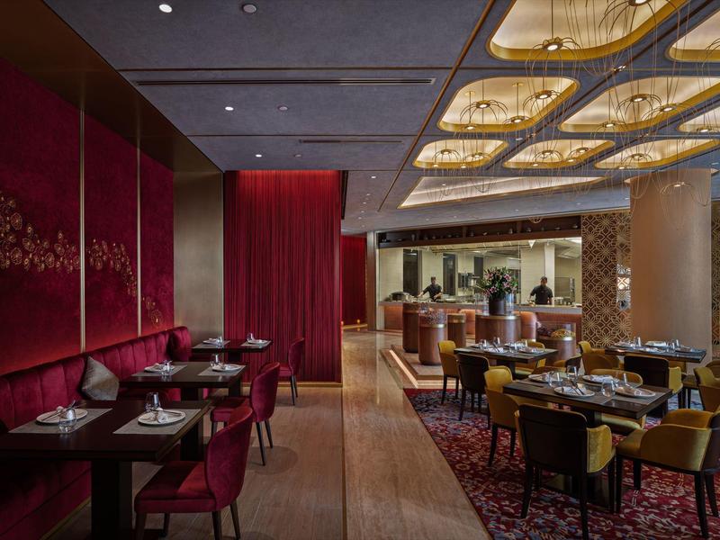 Elegantes Restaurant mit roter und gelber Polsterung, dunklen Holztischen und stilvoller Deckenbeleuchtung.