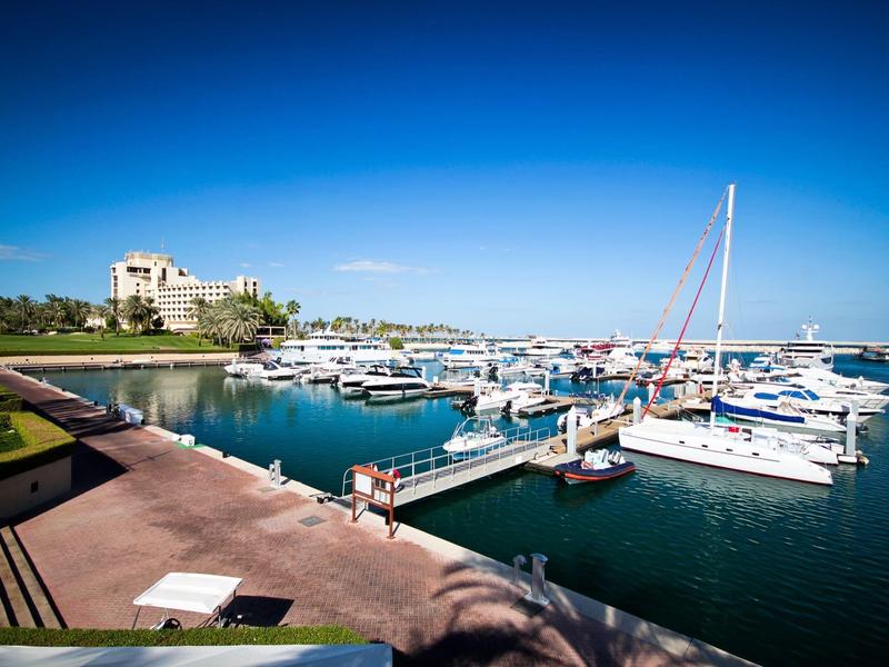 Ein Hafen mit vielen weißen Segel- und Motorbooten bei blauem Himmel und klarem Wasser.
