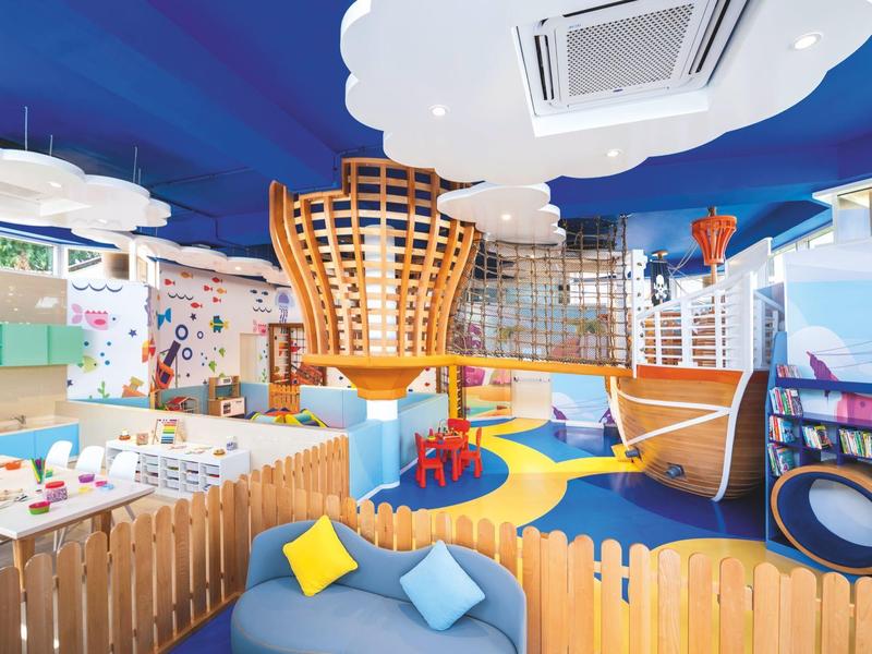 Bunter Indoor-Spielplatz mit Holzkonstruktionen, Klettergerüst, Rutsche und gemütlichem Sitzbereich.