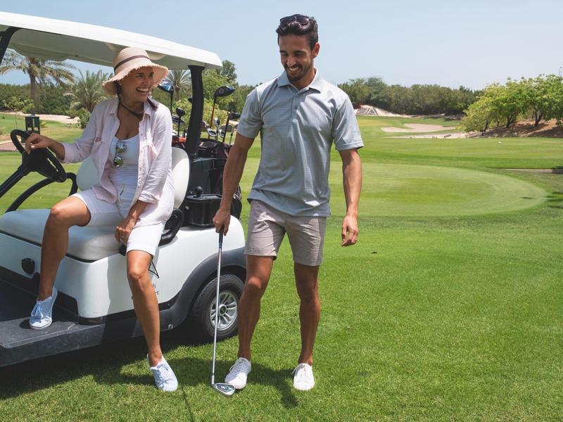 Zwei Männer auf einem Golfplatz, einer sitzt im Golfwagen, der andere steht mit Golfschläger.
