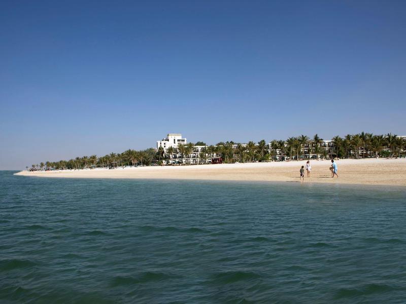 Klarer blauer Himmel, grüner Ozean, weißer Sandstrand mit Palmen und zwei Menschen zu Fuß.