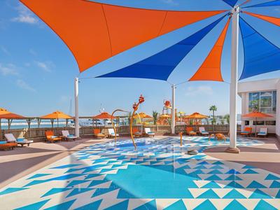 Moderner Swimmingpool mit blau-weißen Fliesen und bunten Sonnenschirmen am sonnigen Tag.