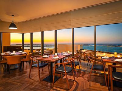 Restaurante con muebles de madera y vista al mar al atardecer a través de grandes ventanas