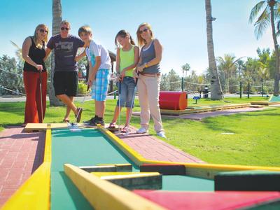 Eine Gruppe von fünf Personen spielt Minigolf auf einem sonnigen, gepflegten Platz mit Palmen.