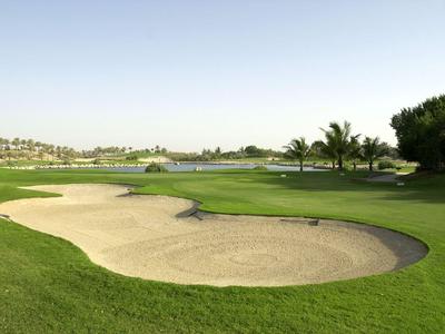 Golfplatz mit Sandbunker, grünen Rasenflächen und Palmen unter klarem Himmel.